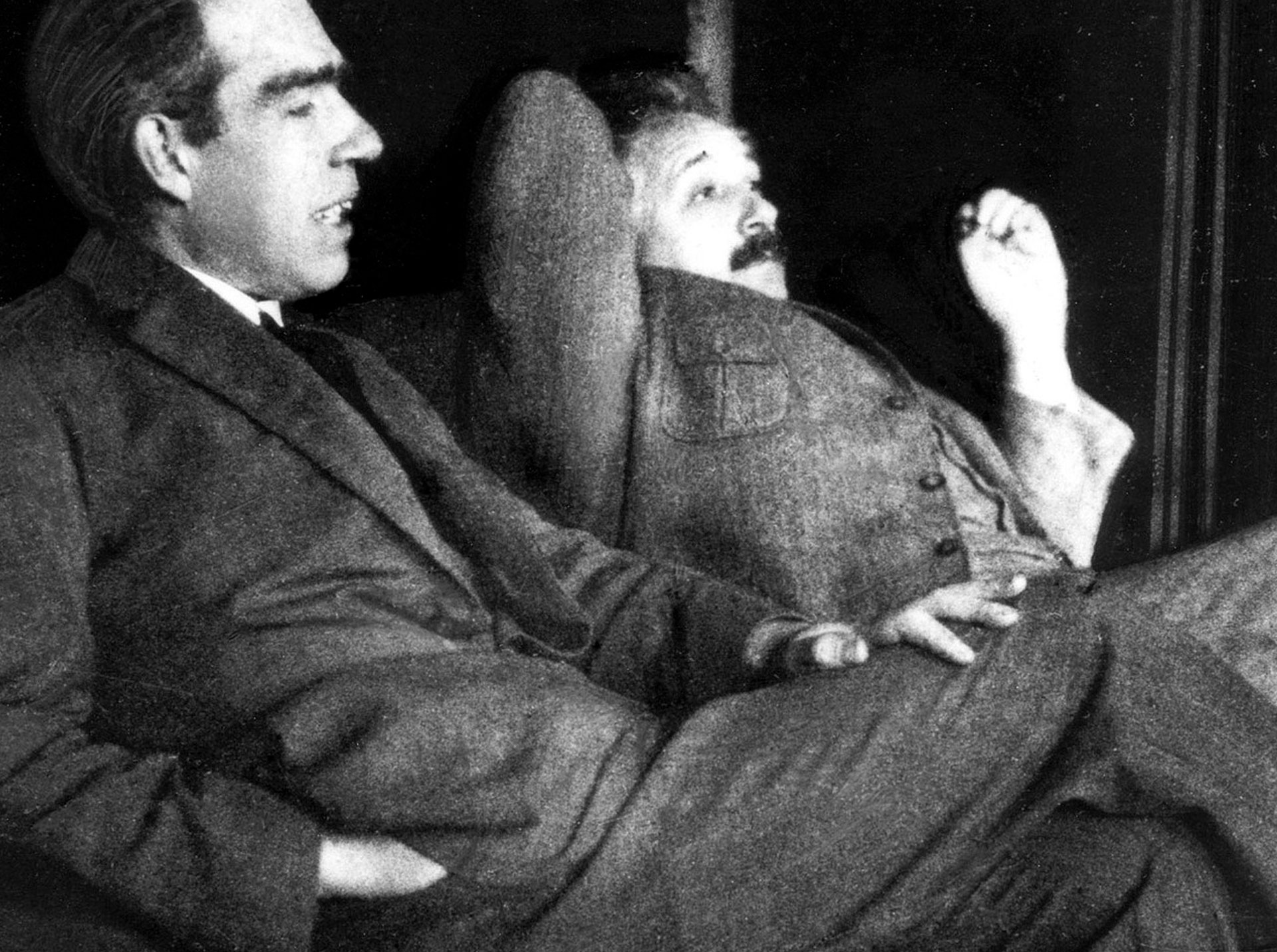 Auf dem schwarz-weiß Foto sind im Vordergrund Niels Bohr und neben ihm etwas im Hintergrund Albert Einstein abgebildet. Beide haben Anzüge an, sitzen lässig angelehnt und scheinen gemeinsam zu philosophieren. Symbol dafür, was die Quantenphysik dazu sagt, wer du bist. 